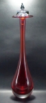Licoreiro, 36cm; grosso cristal contemporâneo, corpo liso em forma de gota, na tonalidade rubi. Tampo arrematado por pinha, incolor. Muito bem conservado.