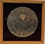 Placa Institucional em metal emoldurada, autoria Dohms Pennas Lia, Dr. Flores 127, med. 33 cm de diâmentro e  com moldura 47 x 47 cm. Estado de conservação bom