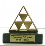 Escultura em metal dourado base em mármore negro com placa em metal "Fenaseg 50 Anos 1951-2001", med. 7 x 8 cm. Estado de conservação bom