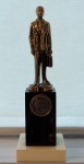Escultura em bronze com base em material sintético "Honra ao Mérito, med. 25 cm. Estado de conservação bom