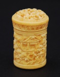 Porta-pílula em marfim oriental esculpido, decorado com pagode e paisagem em sua lateral e com figuras em sua tampa, medindo 33 mm de altura e 20 mm de largura.