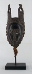 Imponente máscara africana de coleção em madeira entalhada com barba em palha trançada, sobre base em ferro, med. 46 cm
