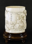 Porta pincéis esculpido em marfim, decorado com figuras e pássaros. Assinado. Acompanha peanha de madeira. Medidas 12 x 9 cm.