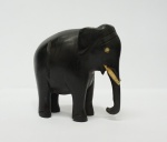 Pequena estatueta africana em formato de elefante em madeira ébano com olhos e presas em marfim, med. 52 x 53 mm.