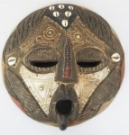 ARTE  AFRICANA. Máscara em madeira policromada, com detalhes em metal e búzios de Gana, medindo 27 cm de diâmetro.