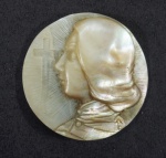Medalha em madrepérola com rosto feminino entalhado e marcada no verso. Diâm. 4 cm