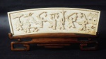 Grupo escultórico em marfim chinês em baixo relevo representando cotidiano. Selo vermelho no verso. Sobre peanha em madeira. Medida: 9x21cm.