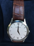 Relógio de pulso masculino. Marca: Baume & Mercier, caixa 35 mm, pulseira de couro marrom, fundo branco, acompanha certificado de garantia e estojo original.