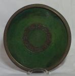 Prato em cerâmica chinesa ao gosto da dinastia Tang, esmalte na cor verde, moldura em bronze e assinatura em relevo na parte inferior medindo 22,5cm de diâmetro.
