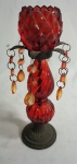 Castiçal em grosso vidro vermelho com guarnições em ferro e pingentes, medindo 26 cm de altura.