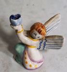 Pequeno castiçal em porcelana no formato de anjo, medindo 12 cm de altura. Apresenta alguns bicados.
