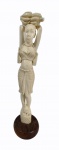Escultura em marfim representando Africana com cacho de banana na cabeça, base de madeira.  Alt.  30 cm.